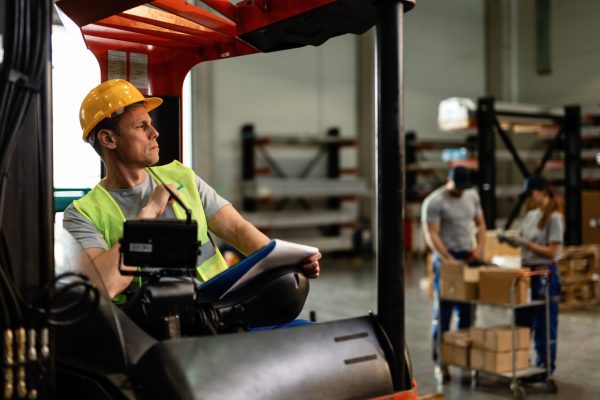 Warehouse forklift driver thinking of something while going through delivery schedule in industrial building.